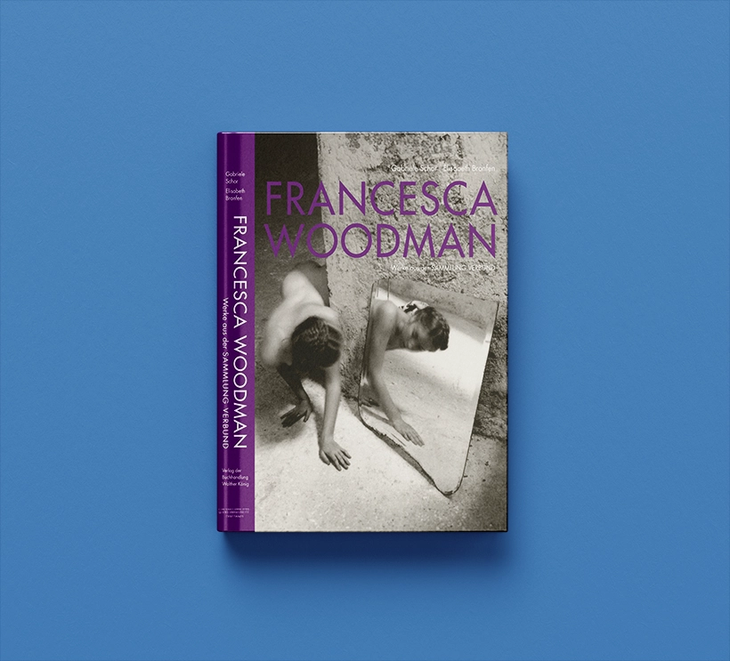 We see Francesca Woodman's catalog raisonné from 2014. The font is in violet. The cover features a black and white photograph of a woman in a rough concrete setting and her reflection in a large shard of mirror.