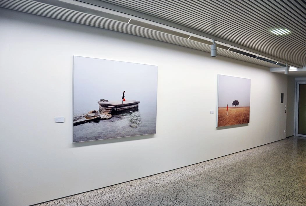 Clean and bright art gallery with two large photographs on a white wall depicting maritime scenes, grey terrazzo floor, and textured ceiling in the room.