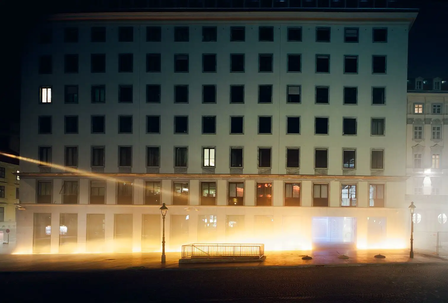 Blick auf das VERBUND-Gebäude am Hof. Es ist dunkel und die Installation von Olafur Eliasson lässt den Platz und das Gebäude zu einer Bühne aus Nebel, Licht und Wind werden.