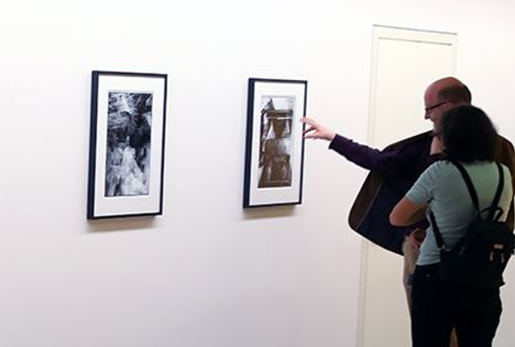 You can see two visitors to the exhibition standing in front of four photographs on a white wall. The photographs are black and white and are in a passepartout frame