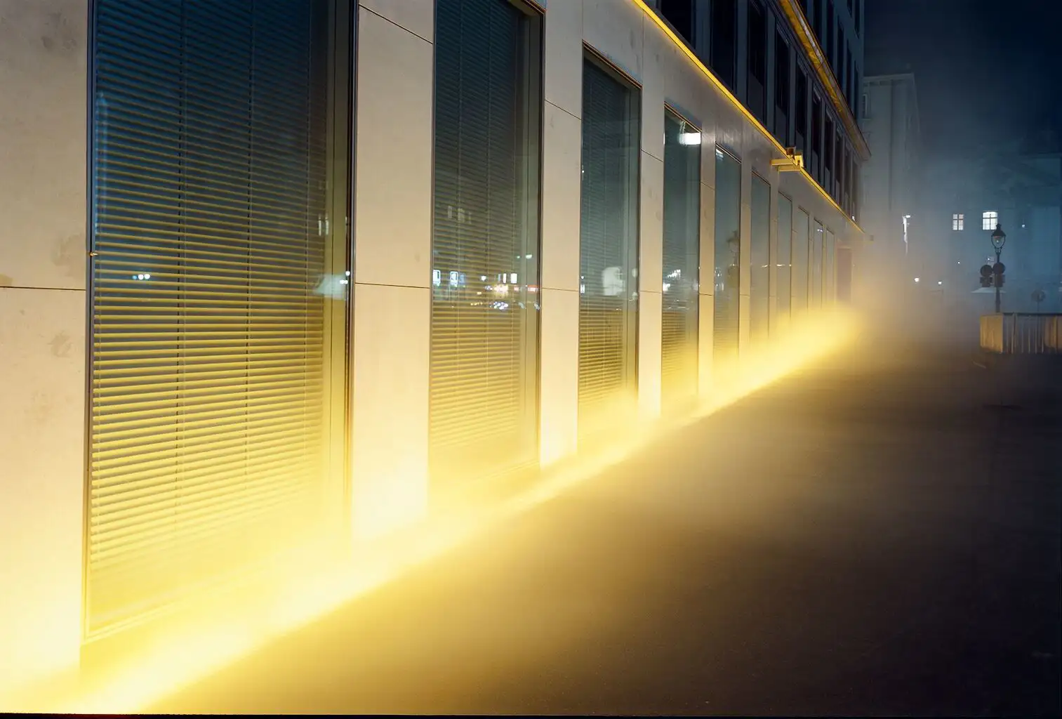 View of the VERBUND building in the courtyard. It is dark and Olafur Eliasson's installation transforms the square and the building into a stage of fog, light and wind.