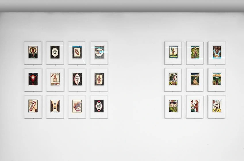 The photograph shows a collection of small-format color prints on a white wall.