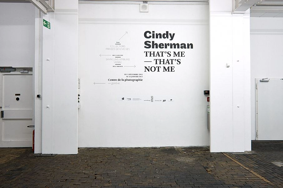 Entrance area of the Cindy Sherman exhibition titled "That's me – That's not me" on the wall of a gallery with a bright interior and cobblestone flooring.