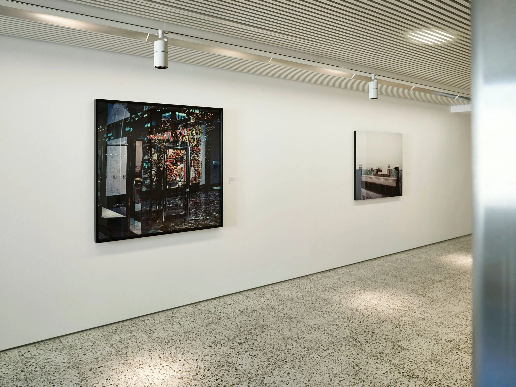 On an office corridor with white walls and a marbled floor hang two large-format photographs.