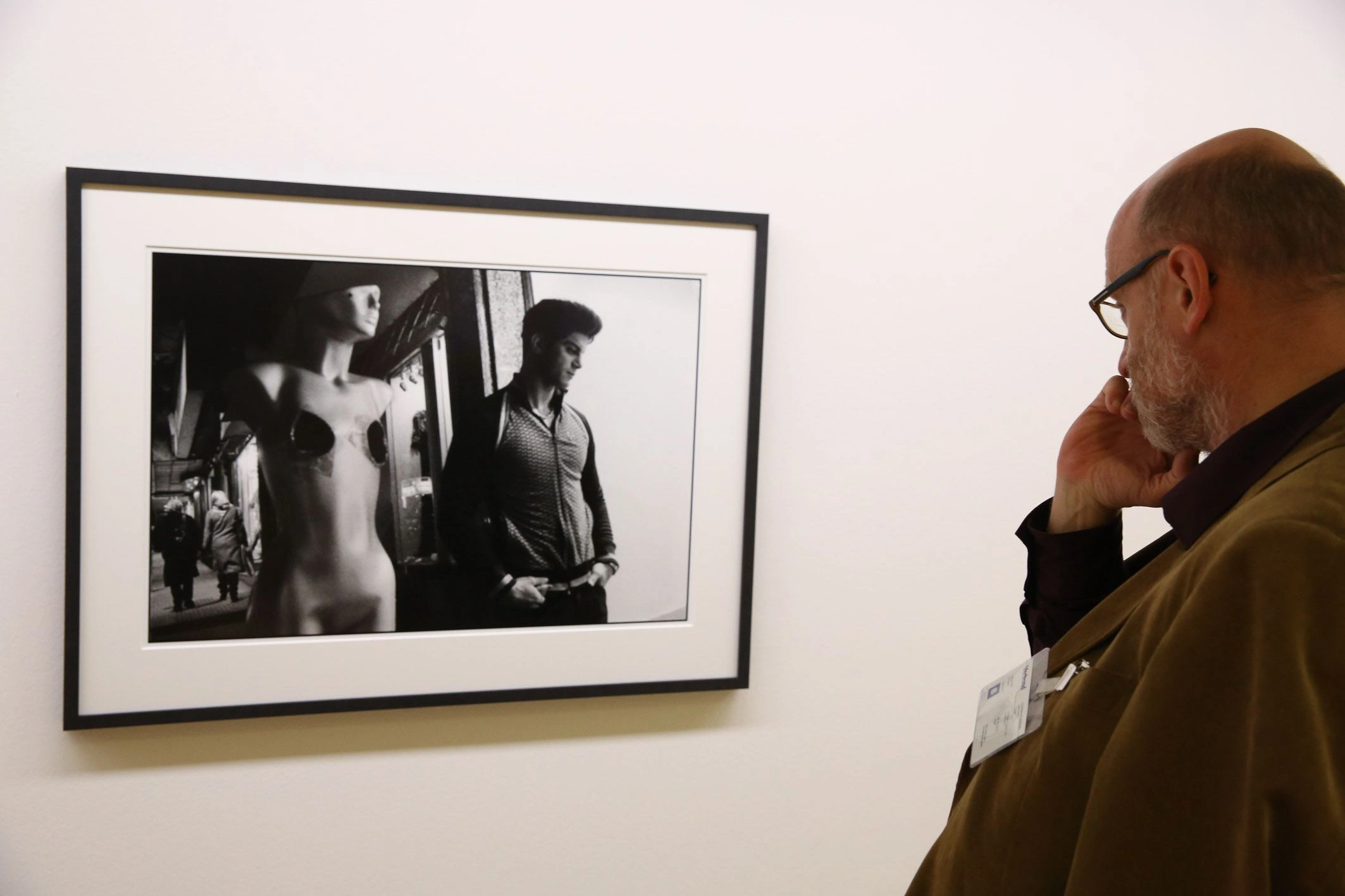 What you see is a black and white photograph on a white wall. A man is standing to the right of it, looking thoughtfully at the work of art.