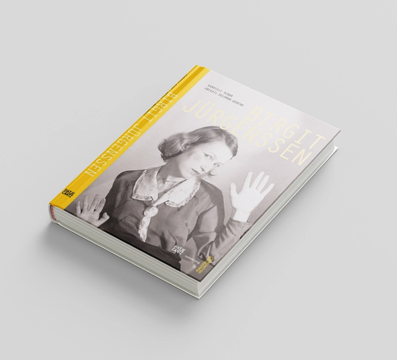 Birgit Jürgenssen's exhibition catalog from 2010 shows a photograph of a woman in black and white pressing herself against a pane of glass. The font and the spine of the book are in yellow.