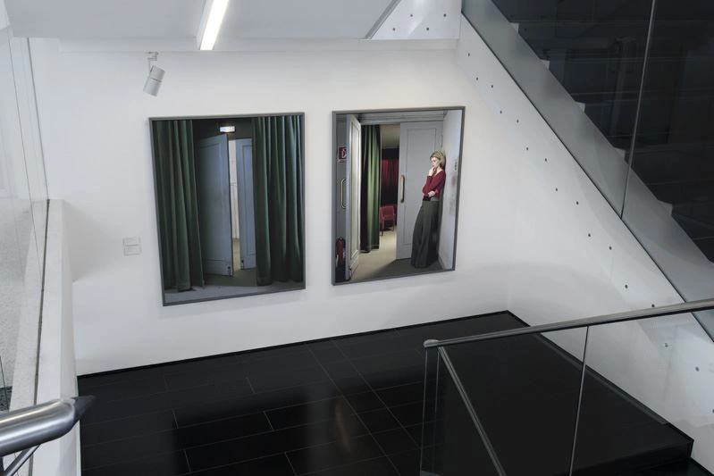 Modern staircase with black floor. Two large, portrait-format pictures hang on a white wall.