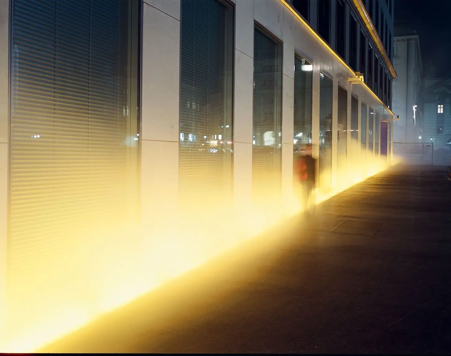 Gelber Nebel steigt neben dem VERBUND-Gebäude auf. Eine schemenhafte Gestalt ist außerdem zusehen. Hierbei handelt sich um den sogenannten Yellow Fog des Künstlers Olafur Eliasson.