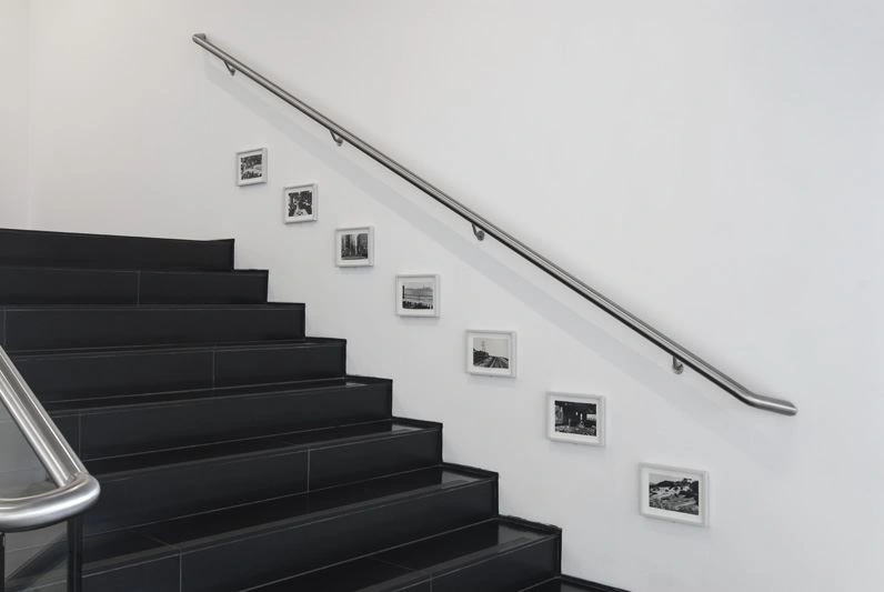 Staircase with black stairs and silver handrail. Seven black and white photographs in landscape format are hung under the handrail