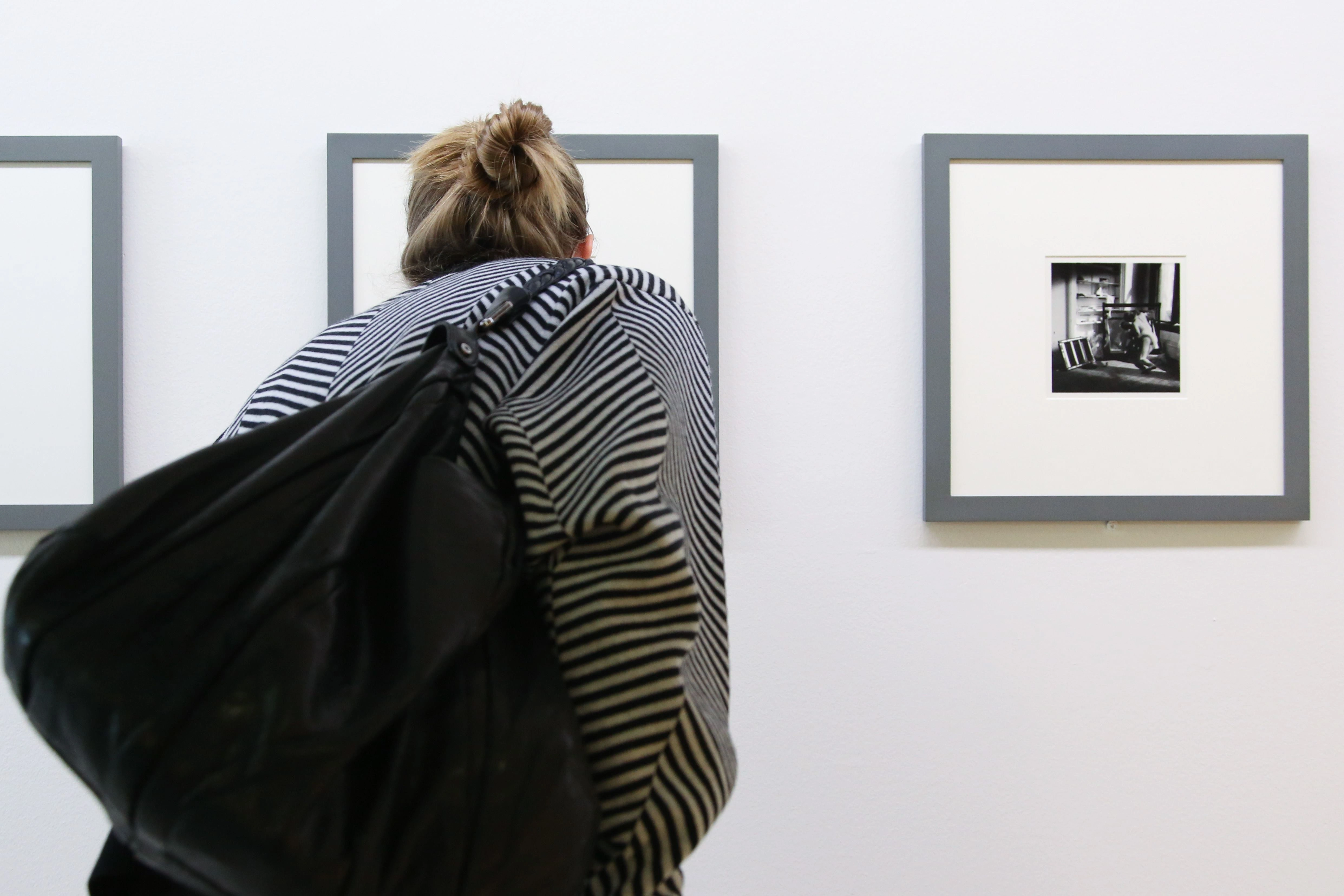 A visitor is seen from behind bending over a painting to take a closer look.