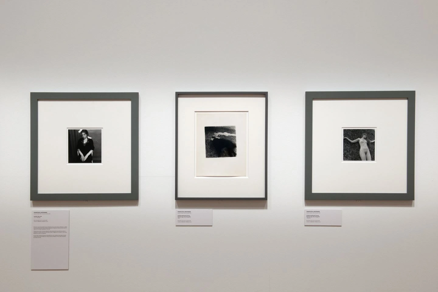 A white exhibition wall can be seen with three square picture frames. Inside are photos of Bozar in black and white. Below them are signs with explanations of the artworks.