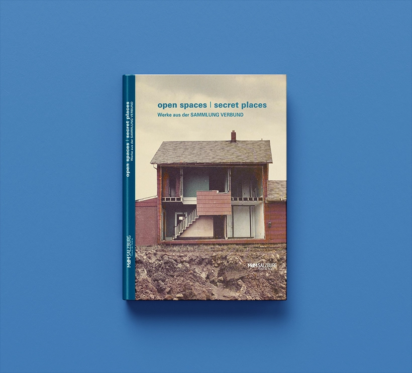 Wir sehen den Ausstellungskatalog von open spaces / secret places aus dem Jahr 2012. Das Cover zeigt direkte Einblicke in eine Einfamilienhaus. Hierbei wurde eine Seitenwand entfernt, so das der Betrachter in das Innere des Hauses blicken kann.