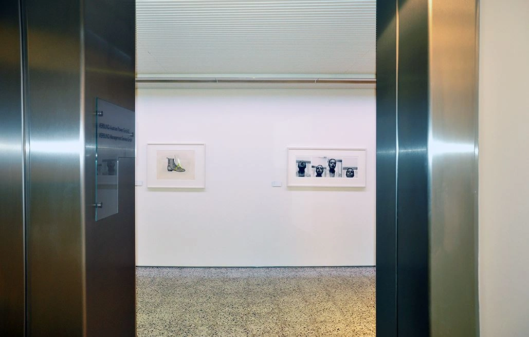 View through an open door at a display wall with two framed pieces of art by Birgit Jürgenssen in the 2009 Sammlung Verbund exhibition, minimalistically presented against a white wall.