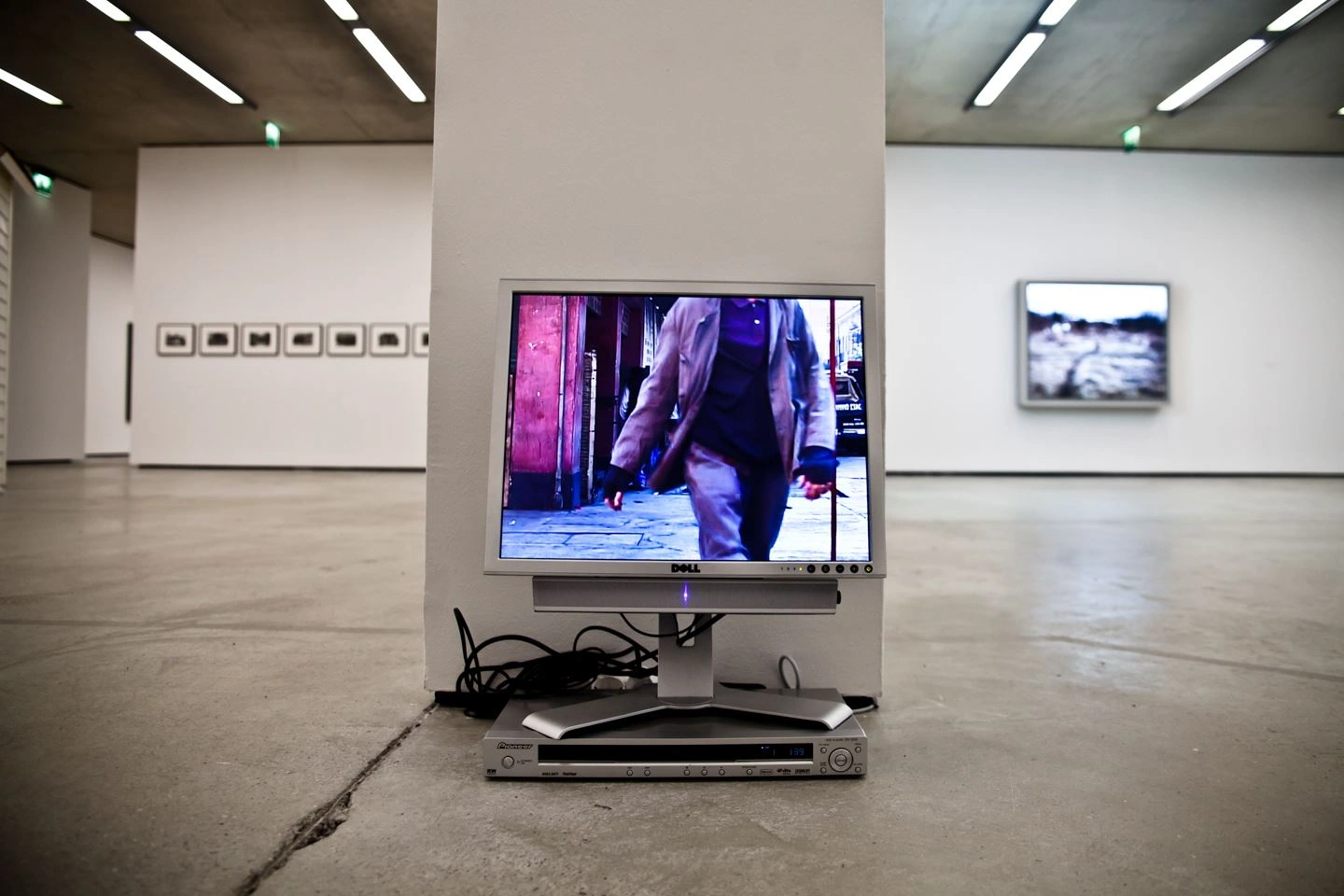 Monitor displaying video installation in an art gallery with additional photographs on the white walls in the background.