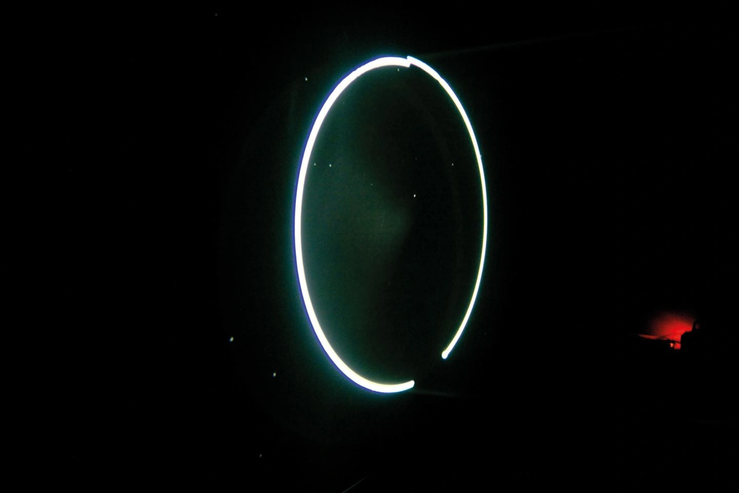 A glowing white circle appears against a black background, possibly a light installation in a dark room.