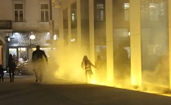 View of the VERBUND building in the courtyard. It is dark and Olafur Eliasson's installation transforms the square and the building into a stage of fog, light and wind. A child moves through the fog.