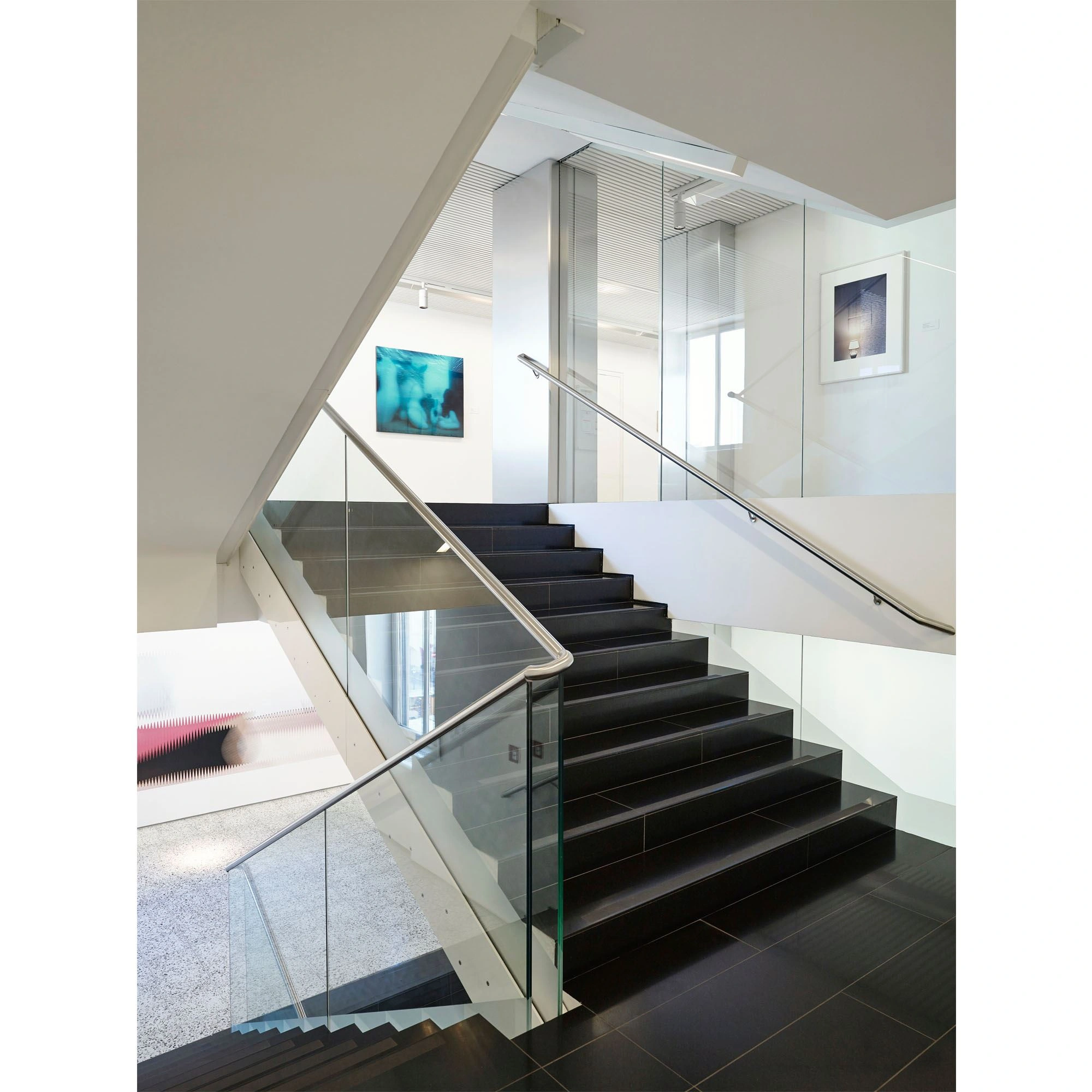 You can see a modern staircase with a glass handrail and black stairs with tiles. On the walls of the corridors hang large-scale abstract works of art.