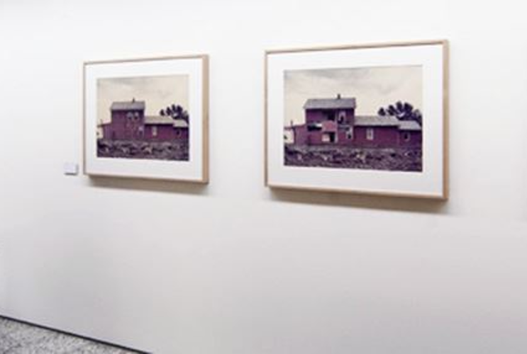 On display is a white gallery wall with several smaller photographs. An installation stands in front of it.