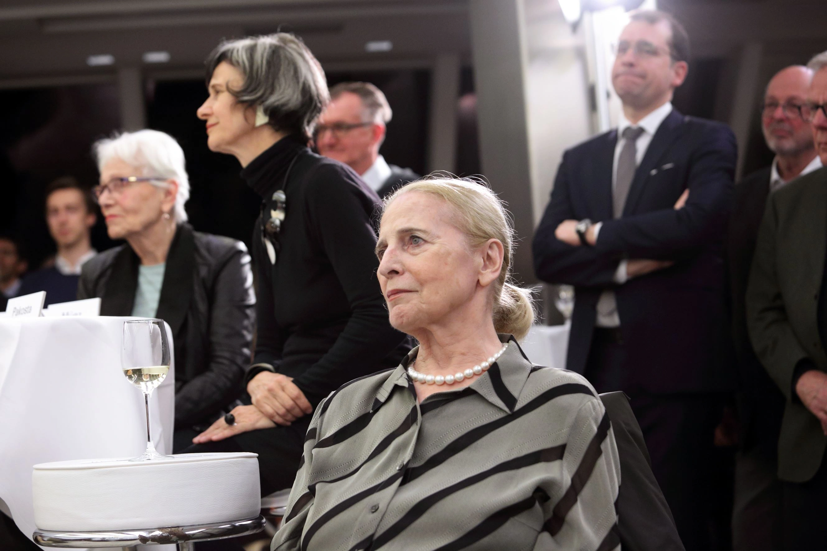 Numerous interested people were present at the press conference for the exhibition opening. An elderly lady with blonde hair sits in the spotlight.